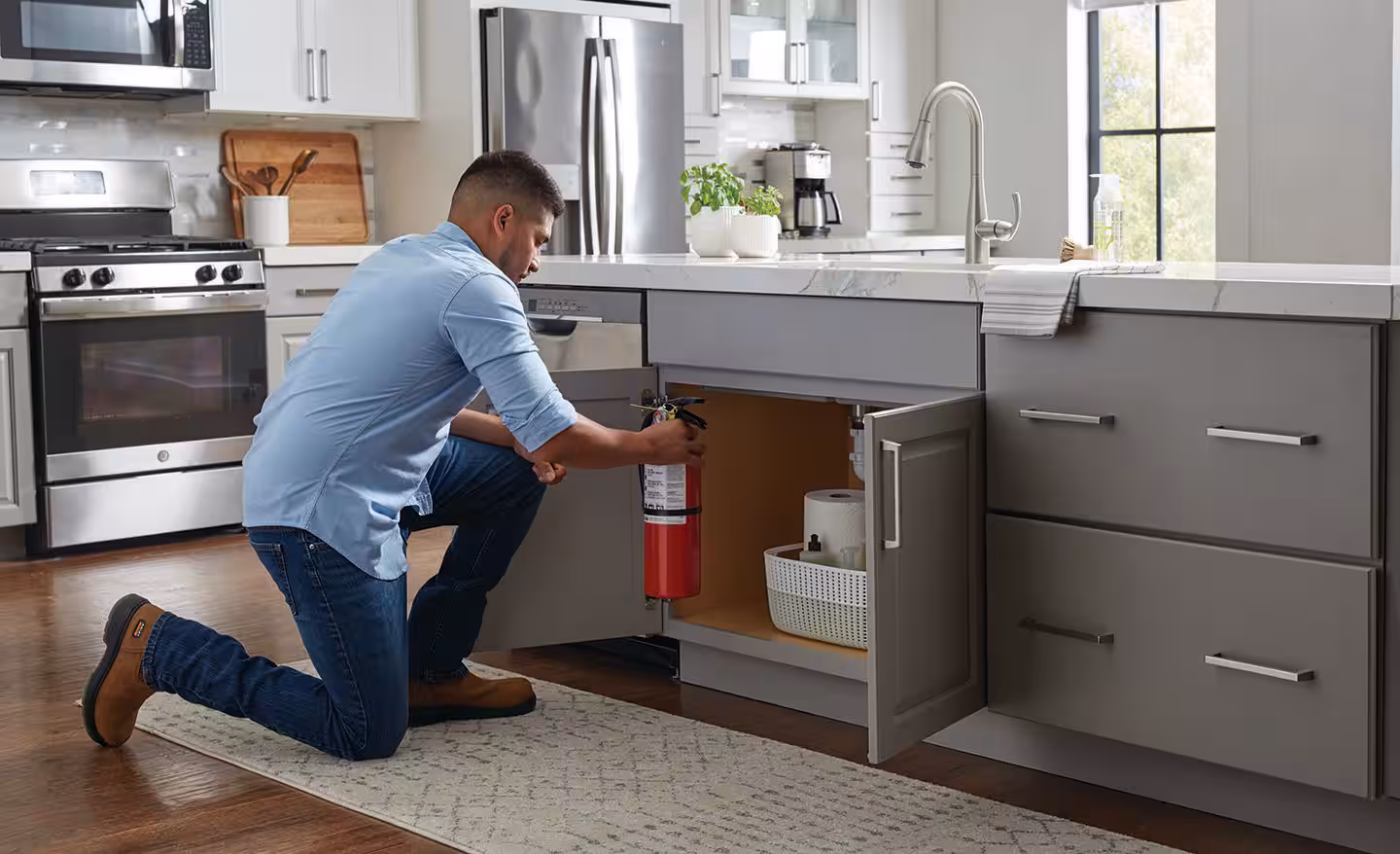 Man placing a fire extinguisher under a kitchen sink for easy access.