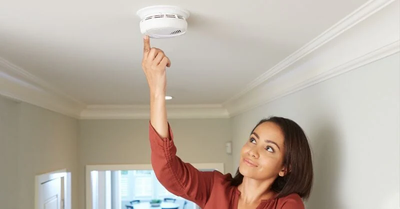 Woman testing a ceiling-mounted carbon monoxide alarm in a home.